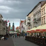 Spacer po Gnieźnie, gdzie widać zabytkowe kamienice, katedrę i ludzi odpoczywających w ogródku piwnym.