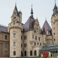 Imponujący moszna zamek zdjęcia, z wieżami i kamiennymi murami, otoczony zielenią.