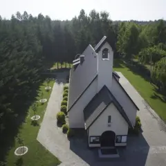 Kościół otoczony lasem, z wieżą i dzwonami. Wokół zadbane alejki i młode drzewka, tworzące urokliwe przypki.