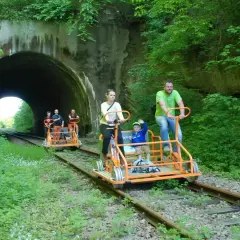 Rodzina na drezynach w Bieszczadach, przejeżdża obok tunelu kolejowego otoczonego bujną zielenią.