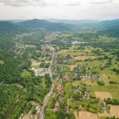Widok z lotu ptaka na malowniczą wieś przytkowice, z domami rozsianymi wśród zielonych pól i lasów, przecinana drogą i rzeką.