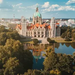 Nowy Ratusz w Hanowerze, stolicy Dolnej Saksonii, odbija się w spokojnej tafli jeziora, otoczony zielenią drzew.