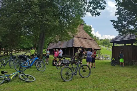 Grupa rowerzystów odpoczywa przy drewnianej cerkwi, planując dalszą podróż po malowniczych trasach rowerowych Bieszczad.