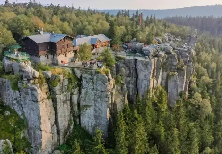 Schronisko na skalnej półce, otoczone lasem, z widokiem na wysokie góry.