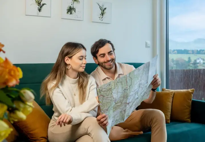 Para planuje podróż, przeglądając mapę. W tle widać krajobraz z domkami, przypominający widok z **Osolina**.