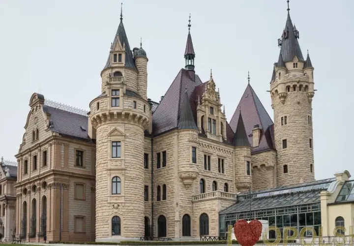 Imponujący moszna zamek zdjęcia, z wieżami i kamiennymi murami, otoczony zielenią.