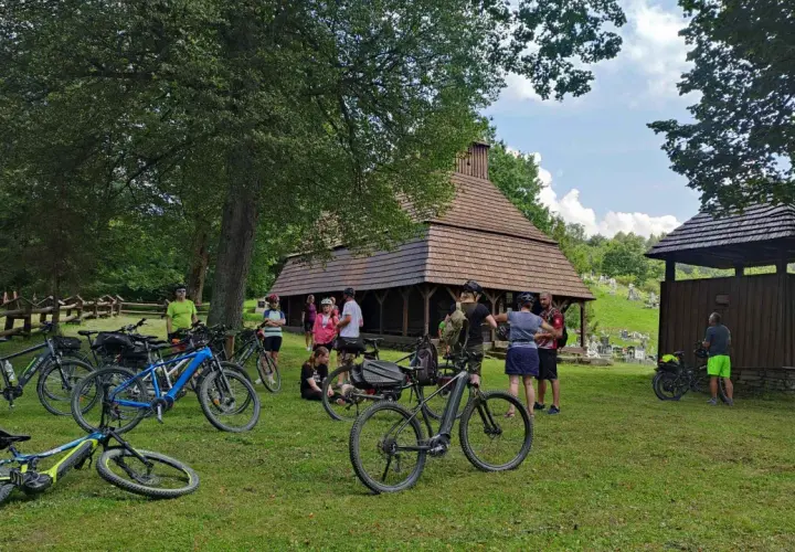 Grupa rowerzystów odpoczywa przy drewnianej cerkwi, planując dalszą podróż po malowniczych trasach rowerowych Bieszczad.