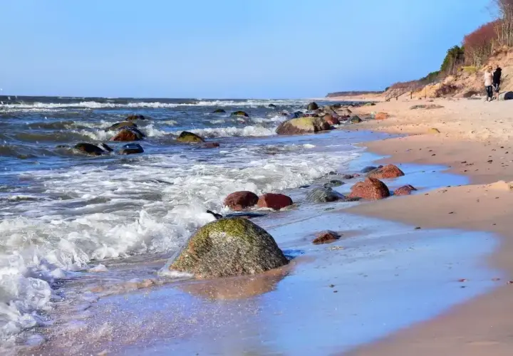 Kamienista plaża nad Bałtykiem, fale rozbijają się o brzeg. Dębina atrakcje to spacer po klifie i podziwianie widoków.