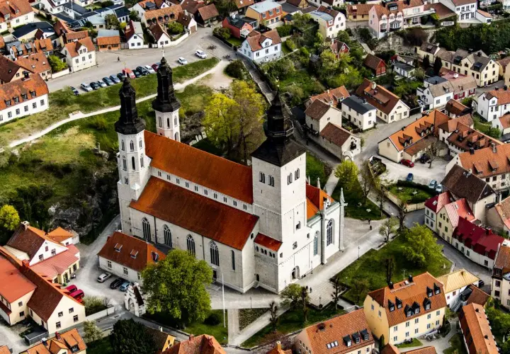 Widok z lotu ptaka na katedrę w Visby, otoczoną zabytkowymi budynkami z czerwonymi dachami.