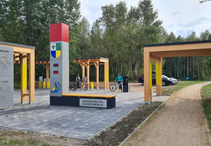 Nowiutka stacja rowerowa na Marszrucie Kaszubskiej. Dwie panie z rowerami, nowoczesna infrastruktura i leśne otoczenie.