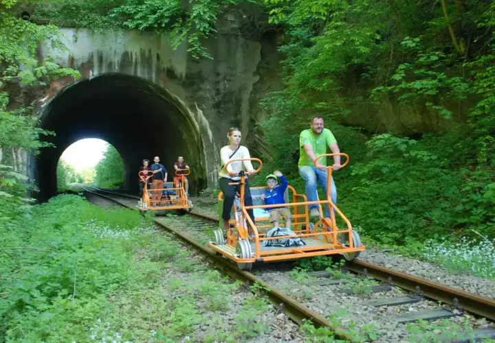 Rodzina na drezynach w Bieszczadach, przejeżdża obok tunelu kolejowego otoczonego bujną zielenią.