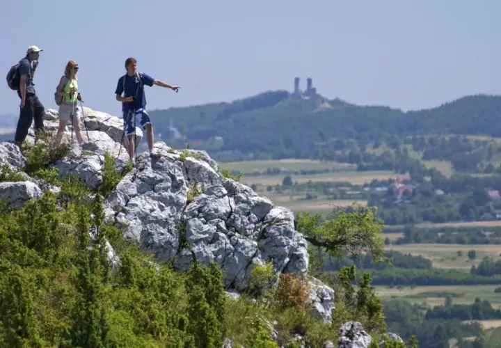 Trzech turystów na skale w Górach Świętokrzyskich, jeden wskazuje kierunek. W oddali ruiny zamku.