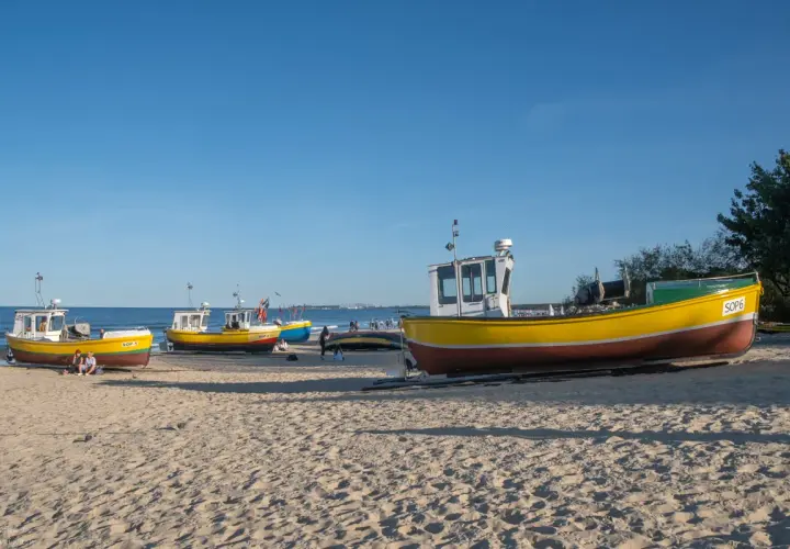 Żółte łodzie rybackie na piaszczystej plaży w Sopocie, spokojne morze i błękitne niebo.