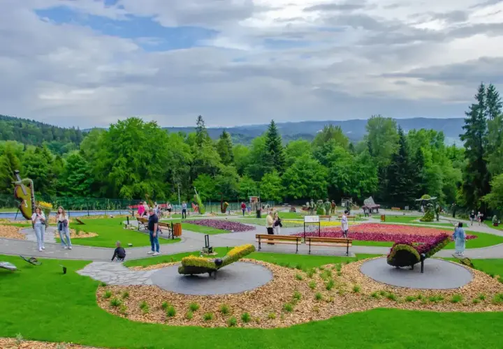 Kolorowy park z rzeźbami z kwiatów i zieleni. W tle las i wzgórza. Sprawdź góra parkowa cennik, by zaplanować wizytę.
