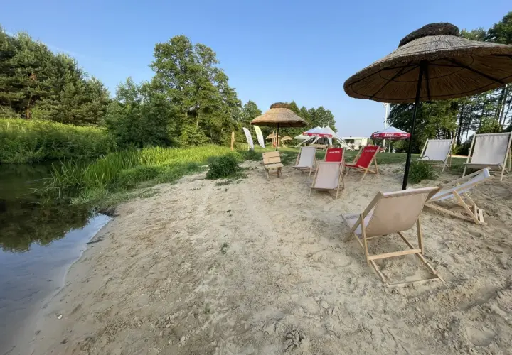 Plaża nad rzeką z leżakami i parasolami. W tle drzewa i niebo. Idealne miejsce na relaks, jak na konopnicy.
