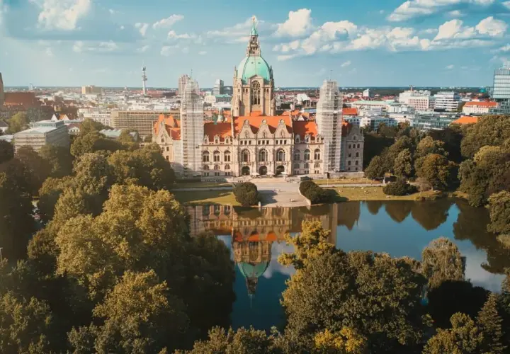 Nowy Ratusz w Hanowerze, stolicy Dolnej Saksonii, odbija się w spokojnej tafli jeziora, otoczony zielenią drzew.