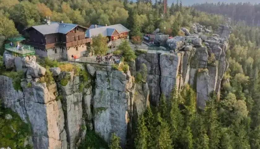 Schronisko na skalnej półce, otoczone lasem, z widokiem na wysokie góry.