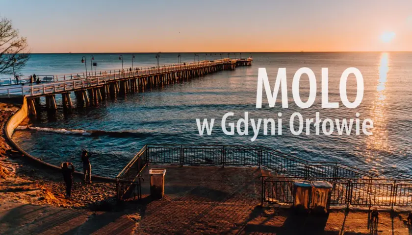 Zachód słońca nad morzem w dzielnicy Gdyni z molo. Długie molo w Orłowie, spokojne fale i dwie osoby na plaży.