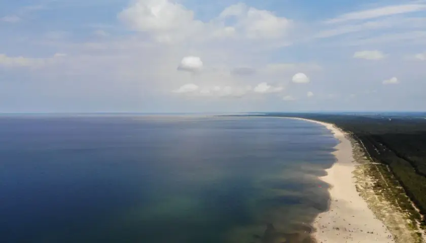 Szeroka, piaszczysta sobieszewo plaża z mnóstwem ludzi wypoczywających nad spokojnym morzem.