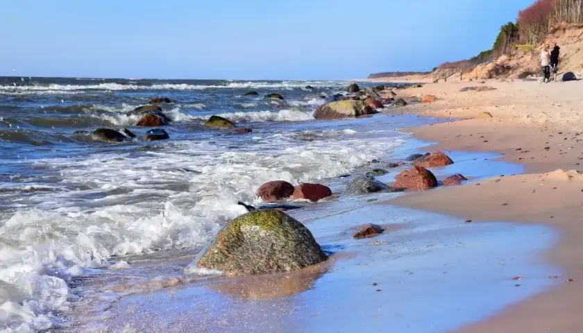 Kamienista plaża nad Bałtykiem, fale rozbijają się o brzeg. Dębina atrakcje to spacer po klifie i podziwianie widoków.