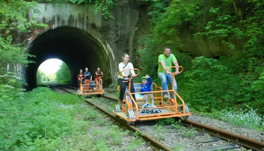 Rodzina na drezynach w Bieszczadach, przejeżdża obok tunelu kolejowego otoczonego bujną zielenią.