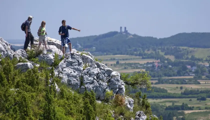 Trzech turystów na skale w Górach Świętokrzyskich, jeden wskazuje kierunek. W oddali ruiny zamku.