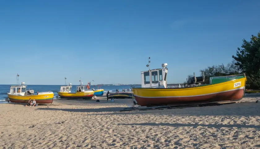 Żółte łodzie rybackie na piaszczystej plaży w Sopocie, spokojne morze i błękitne niebo.