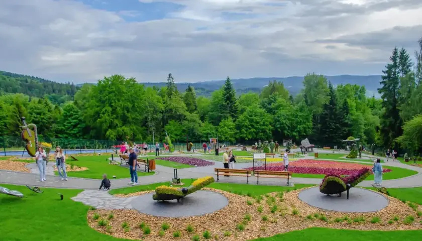 Kolorowy park z rzeźbami z kwiatów i zieleni. W tle las i wzgórza. Sprawdź góra parkowa cennik, by zaplanować wizytę.